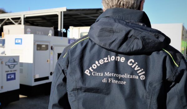 operatore di spalle, sul giubbotto si legge "protezione civile Città Metropolitana di Firenze"; macchine operatrici sullo sfondo