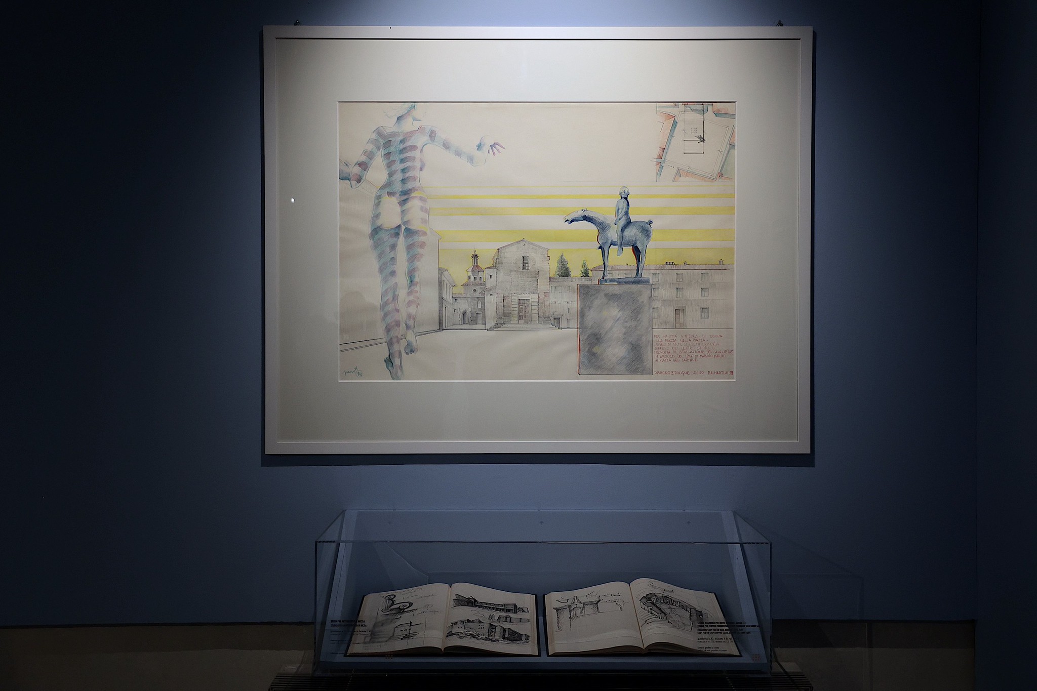 opera dell'artista con cornice bianca, appesa su parete, in basso teca che contiene due libri aperti con disegni dell'artista