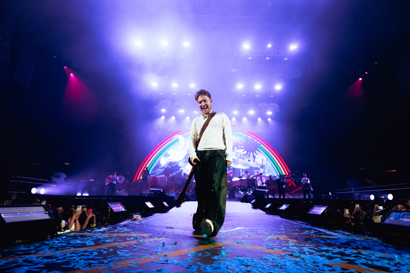 il cantante Alfa su pedana davanti al palco durante un concerto; luci sul soffito e arcobaleno sullo sfondo