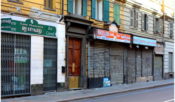 porzione di strada cittadini con portoni e negozi con bandoni abbassati