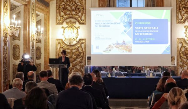 la consigliera sara di maio nel salone degli specchi in piedi al leggio, tavolo dei relatori sullo sfondo, alle loro spalle grande monitor su cui è proiettata slide