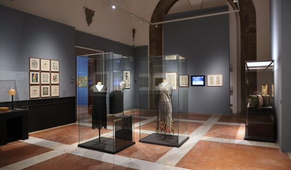 Una sala della mostra Firenze Decò con teche con abiti e quadri alle pareti