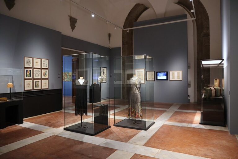 Una sala della mostra Firenze Decò con teche con abiti e quadri alle pareti