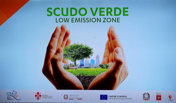 due mani che contengono una città con alberi e prato, scritta "Scudo Verde Low emission zone"