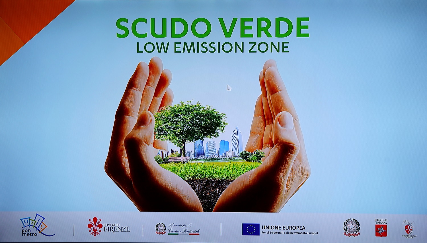 due mani che contengono una città con alberi e prato, scritta "Scudo Verde Low emission zone"