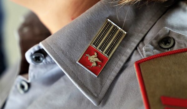 dettaglio del colletto della divisa della Polizia Metropolitana: camicia grigia con spilla con Pegaso su sfondo rosso